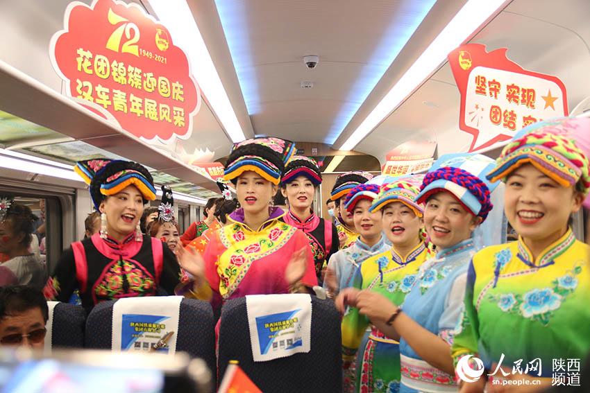 2021年9月30日，陽(yáng)平關(guān)至安康跑起“復(fù)興號(hào)”動(dòng)車組，標(biāo)志秦巴深處的陽(yáng)安鐵路全線邁入動(dòng)車新時(shí)代。圖為陽(yáng)平關(guān)至安康“復(fù)興號(hào)”動(dòng)車上，沿線羌族群眾唱羌歌跳羌舞，用美妙的歌聲迎國(guó)慶。全超雷攝
