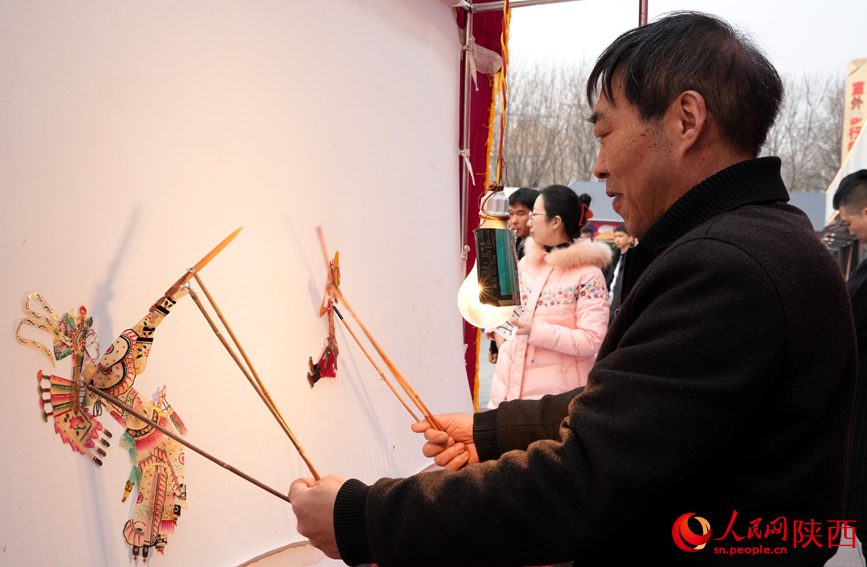 非遺傳承人在燈下演繹皮影戲。人民網(wǎng)記者 賈凱璐攝