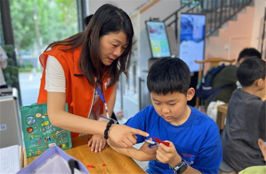 7月18日，志愿者在西安市未央?yún)^(qū)中海開(kāi)元壹號(hào)社區(qū)的托管班上指導(dǎo)孩子學(xué)習(xí)剪紙。未央?yún)^(qū)委宣傳部供圖